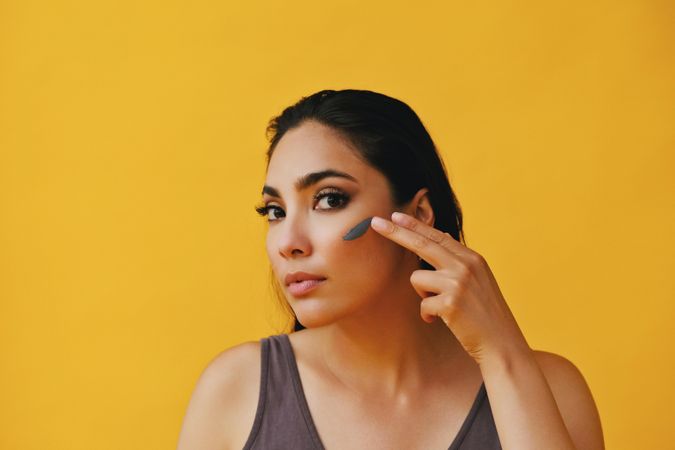 Beautiful Latina woman applying clay mask with hand