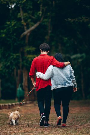 Back view of a couple walking the dog in the woods during daytime