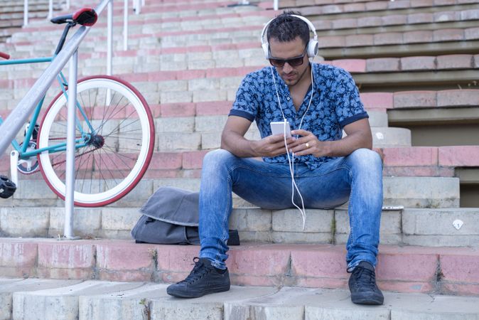 Male cyclist in jeans and blue shirt listening to music on smartphone