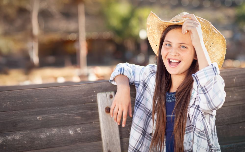 Girl Wearing Cowboy Hat Enjoying The Pumpkin Patch on a Sunny Fall Day.
