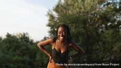 A young Black woman with braids in her hair laughs during a walk in the park at sunset 0WOOqM