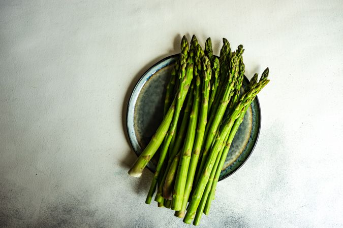 Loose raw asparagus on plate on marble counter with copy space