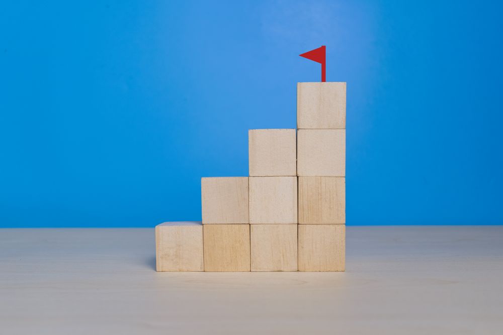 stack staircase wooden blocks with a flag at the top on blue background