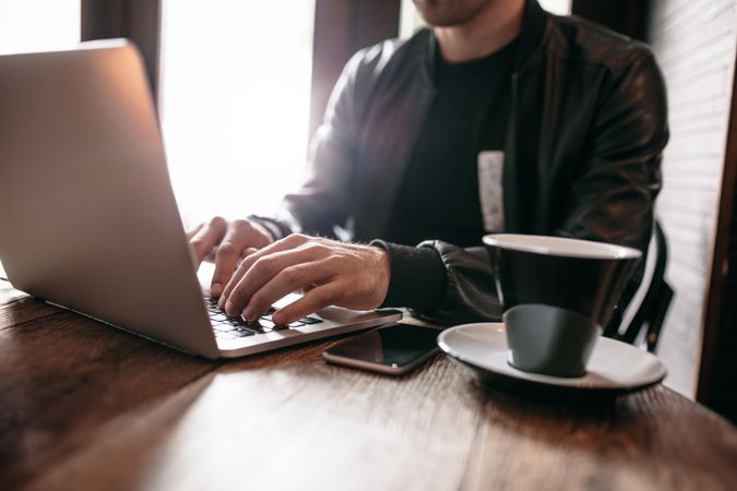 Crop of man at cafe table with coffee and laptop