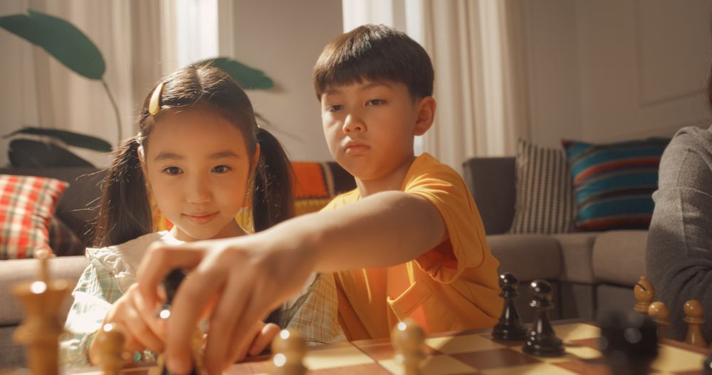 Happy Korean Family Spending Time Together at Home: Young Parents Playing a Game of Chess With Their Cute Children and Having Fun.