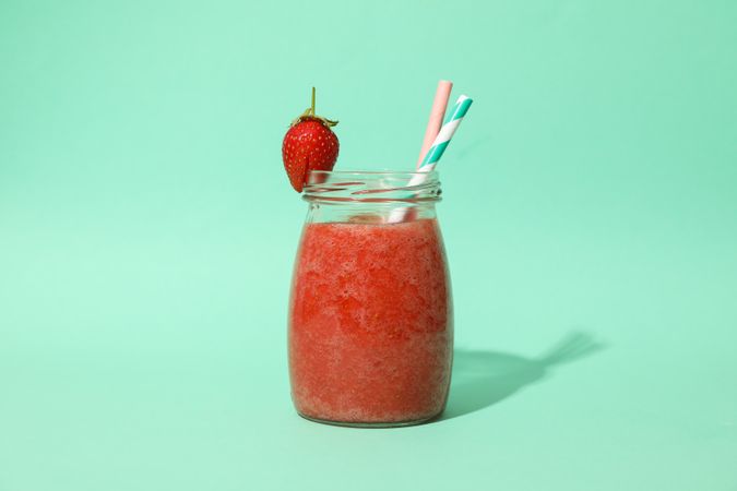 Glass jar with strawberry cocktail on mint background. Summer drink