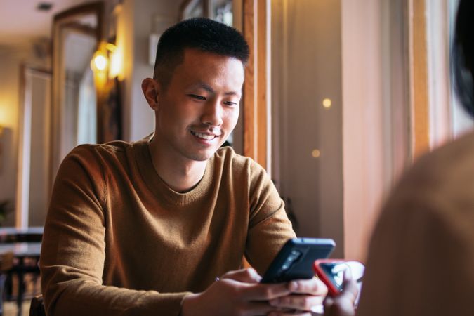 Asian man sitting in coffee shop using smartphone.