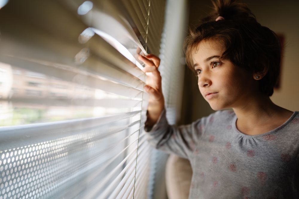 Girl in pajamas standing beside window curtain