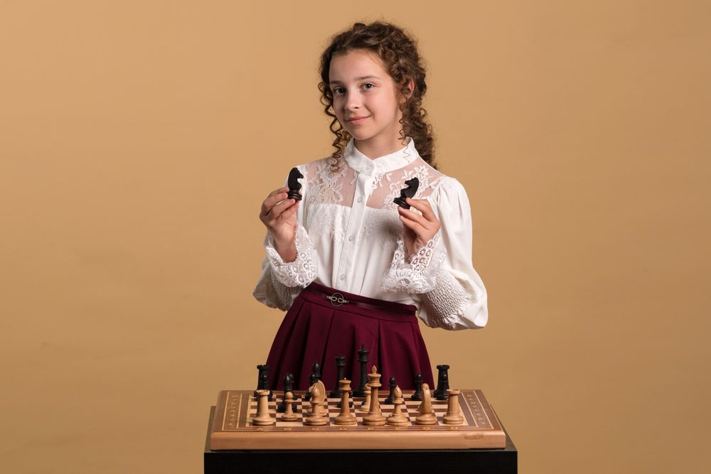 Young girl displaying two chess knights confidently.