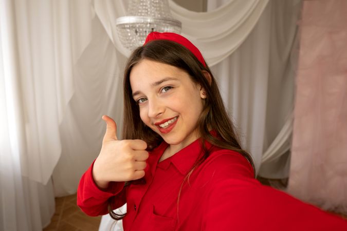 Teen girl smiling giving thumbs-up gesture in selfie photo.