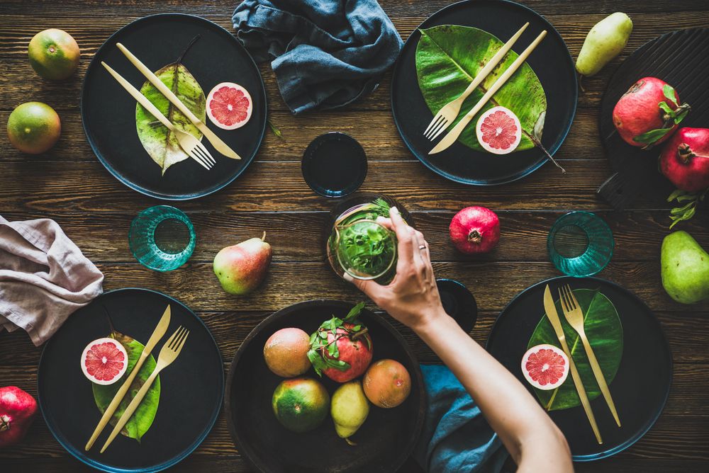 Fresh table setting with leaves on dark plates, fruit with person reaching for pitcher