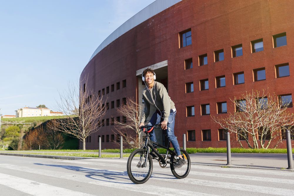 Young happy Black man in headphones riding bicycle