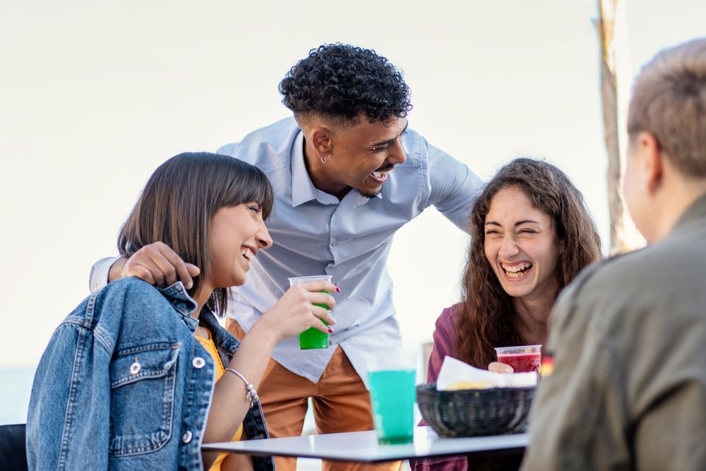 Multicultural friends sharing laughter over colorful drinks at beachside cafe