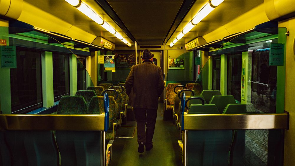Back view of an older man with a hat standing between train's seats