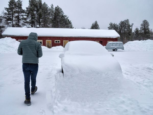 Man walking past car piled with snow