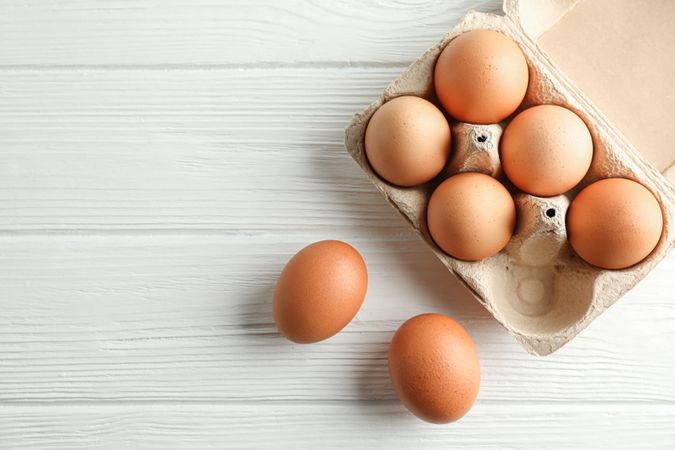 Brown chicken eggs in carton box on light background, space for text and top view