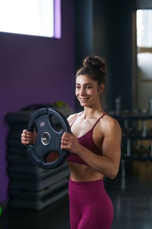 Muscular woman in fitness gear smiling while holding a weight