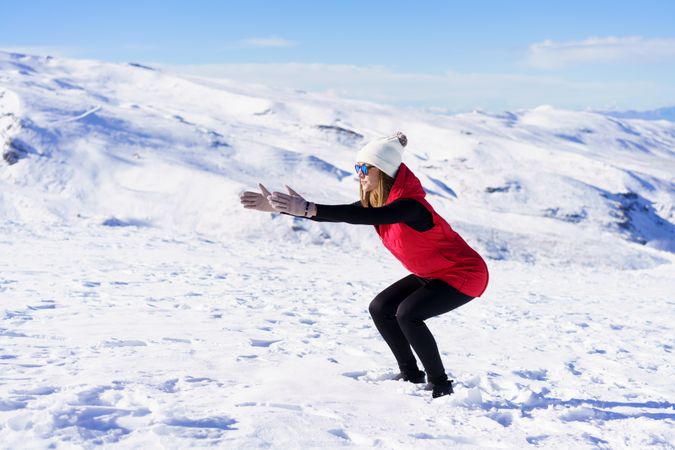 Woman in snow gear doing squats on snowy mountain