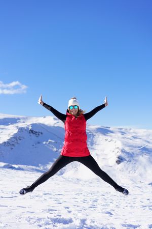 Happy woman in winter gear doing a star jump on snowy mountain