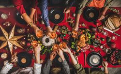 Group of people toasting with drinks at festive red table with cake, roast chicken, and decorations