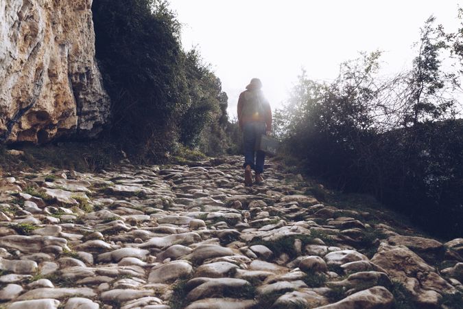 Woman with case walking on rocks above stream