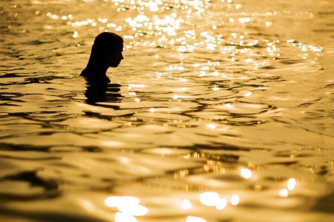 Anonymous woman standing in sea in sunset