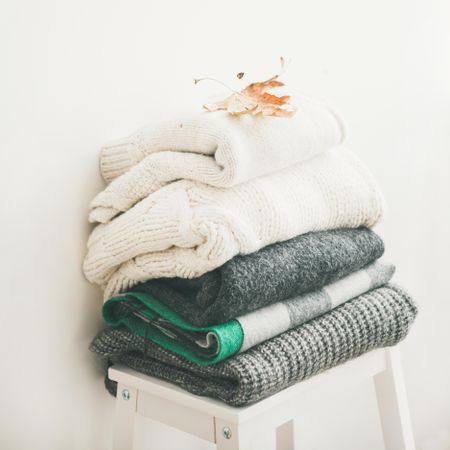 Pile of clean, folded sweaters on light background, square crop