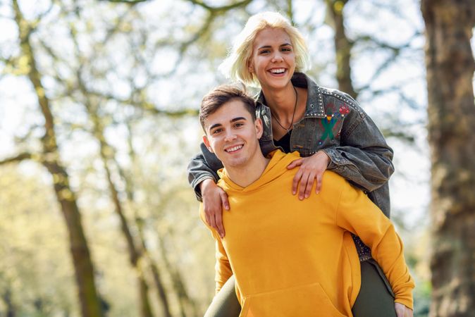 Smiling man giving blonde girlfriend piggy back in park