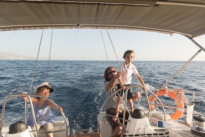 Man with boy and girl holding steering wheel on yacht on water