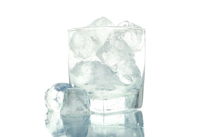 Square rocks glass full of ice, with one cube on table