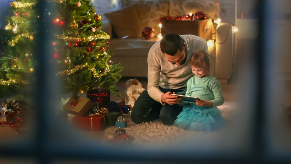 Looking Through the Window at Father Reading Book to His Daughter, Sitting Under Christmas Three with Gifts.