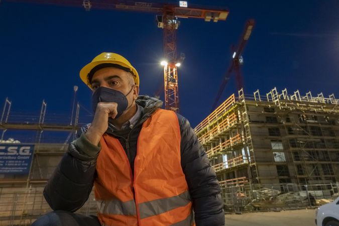 Engineer with facemask beside a building under construction worker at night