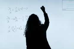 Back view silhouette of a math teacher writing on light board in classroom 0KRa7b