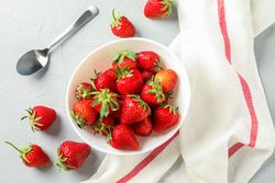 Plate with fresh strawberries, spoon and kitchen towel on bright background, top view