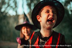Boy howling with laughter in halloween costume with sister in background 5677P4