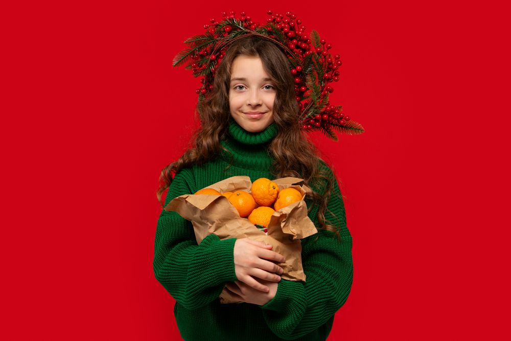 Young girl in green sweater holding paper bag of oranges