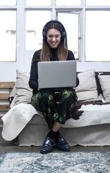 Woman sitting on sofa and using laptop listening to headphones