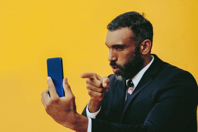 Stern Black businessman in suit speaking at smartphone screen while pointing