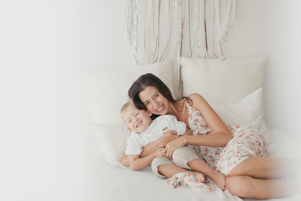 Mother ticking little son and laughing on bed