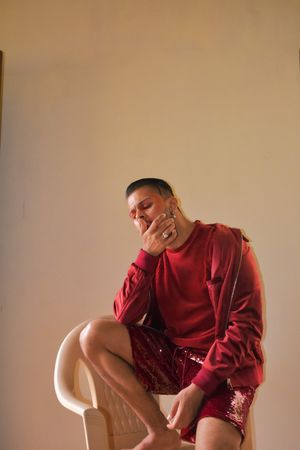 South Asian man in red shirt and shorts putting a foot on plastic chair