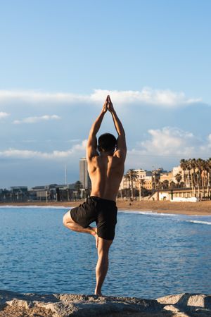 Shirtless man balancing in yoga pose on beach