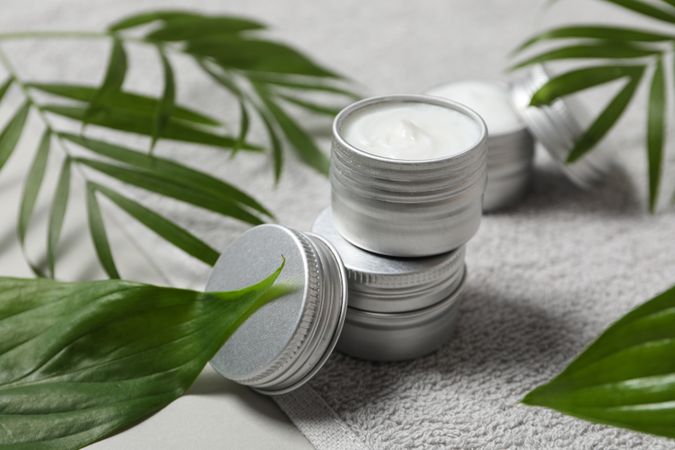 Jars with cream on towel and leaves on gray background