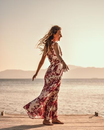 Woman in red floral sleeveless dress standing on wooden dock on beach