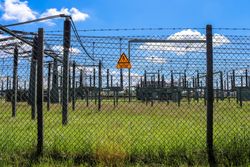 Sign showing the words high voltage in german language at the fence of a big substation distributing electric energy with lots power lines on a sunny day