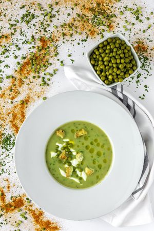 Green vegetable cream soup with crackers and peas in bowl