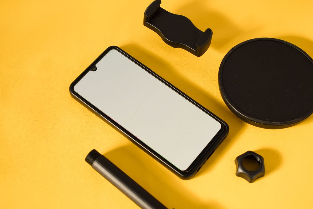 Phone with mockup screen and accessories scattered on yellow table with shadow and space for text
