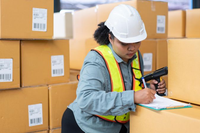 Woman in safety gear working in distribution center checking bar codes on boxes