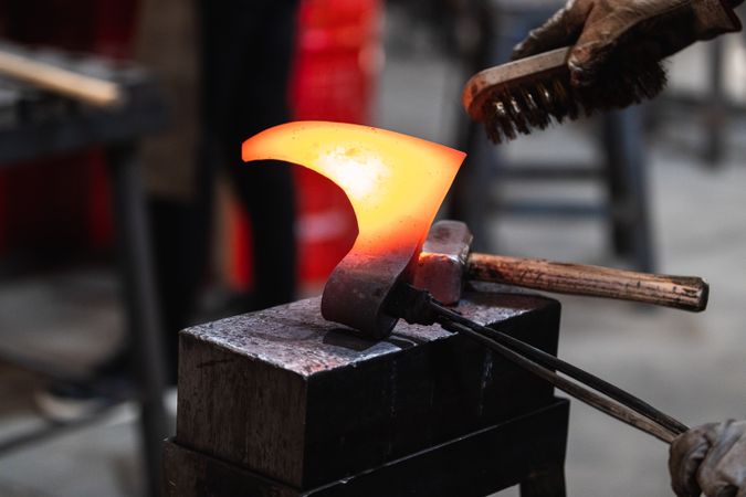 Artisan with wire brush and pincers forging metal axe