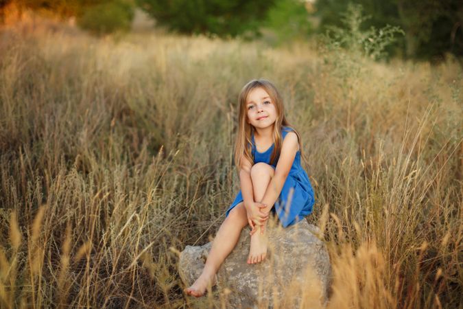 Female child sitting on bolder in field