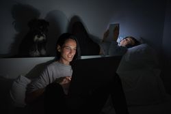 Woman and boy using gadgets near Miniature Schnauzer at night